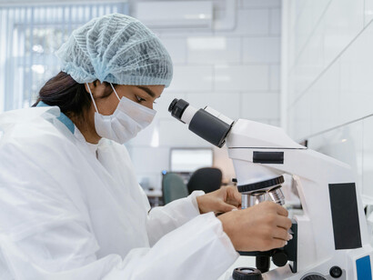 Scientist wearing a mask examines samples under a microscope in an AI-supported laboratory