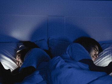 A couple in bed, illuminated only by their phone screens