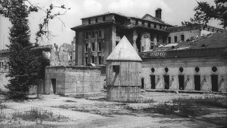 Foto de julho de 1947 da entrada dos fundos do Führerbunker no jardim da Chancelaria do Reich. Os corpos de Hitler e Eva Braun foram queimados em um buraco de granada em frente à saída de emergência à esquerda; a estrutura em forma de cone no centro servia para ventilação e como abrigo contra bombas para os guardas. Hitler sabia e sentia. O seu corpo já ia exangue. As suas mãos, trêmulas. O seu braço esquerdo, imóvel. Os seus olhos, sem vida. O seu semblante, envelhecido. Preocupando os seus convivas. Dos mais jovens aos mais vividos. Acabrunhando inclusive o seu médico, o doutor Morel, que nada conseguia explicar daquela deformação física tão acelerada