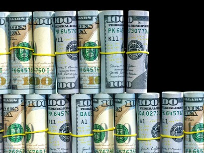 Rotoli di banconote da 100 dollari avvolti con elastici gialli, disposti in due file su sfondo nero
