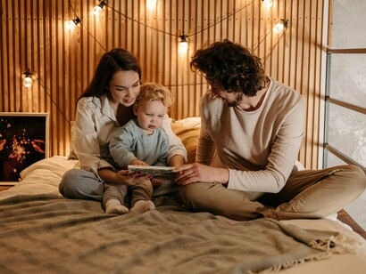 Parents showing their toddler a book, representing the need to introduce young kids to books at an early age to stimulate their imagination, and foster a curiosity for learning about themselves and the world
