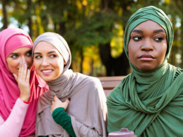 An isolated, unhappy woman stands apart as unkind friends converse nearby