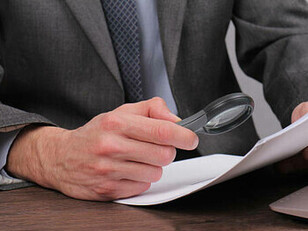 A reporter inspecting a document closely with a magnifying glass as part of the fact-checking process