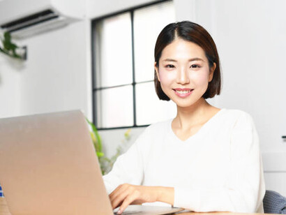 A young Asian woman smiling while working on her laptop