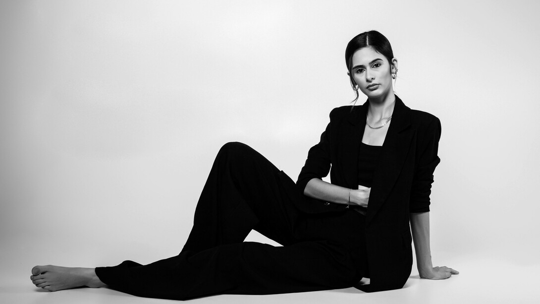 A portrait of a female model posing confidently in a studio, dressed in a sleek black suit that embodies modern sophistication and timeless style