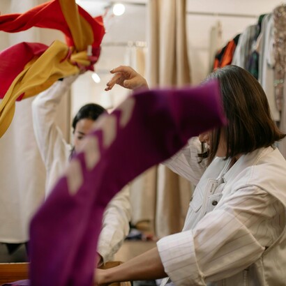 Two friends rummage through racks of secondhand treasures at a bustling thrift store, a treasure hunt of secondhand fashion where every piece carries a story