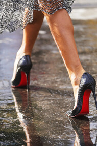 Mujer camina sobre un charco de agua calzando los típicos tacones con suela roja de la marca del diseñador Christian Louboutin