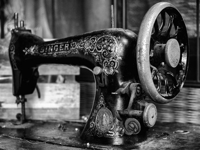 A black and white close-up of a vintage Singer sewing machine visually represents the foundational technological innovation that revolutionized garment production in the 19th century