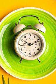On a colored background, a plate with an alarm clock and measuring tape, symbolizing the diet concept and weight loss plan, including intermittent fasting