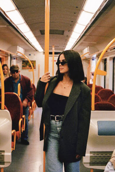 A Gen Z girl, sporting a blazer and vintage sunglasses, effortlessly merging classic and contemporary looks on the train