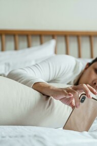 An Asian woman lying in bed while using her smartphone