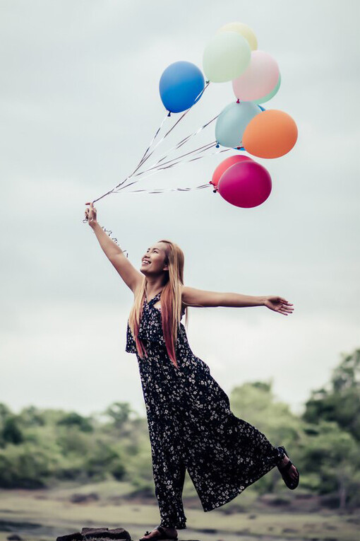 A young woman holding colorful balloons in nature, embracing simple joys, self-care, and relaxation, with sunlight gently warming her skin