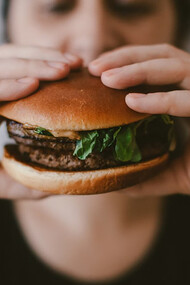 A person holding a large, juicy burger with both hands