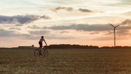 A man cycles near a wind turbine, symbolizing the connection between sustainable living and renewable energy