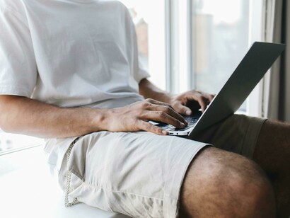 Gen Z man sitting in front of a laptop while scrolling on his phone, multitasking in a digital workspace