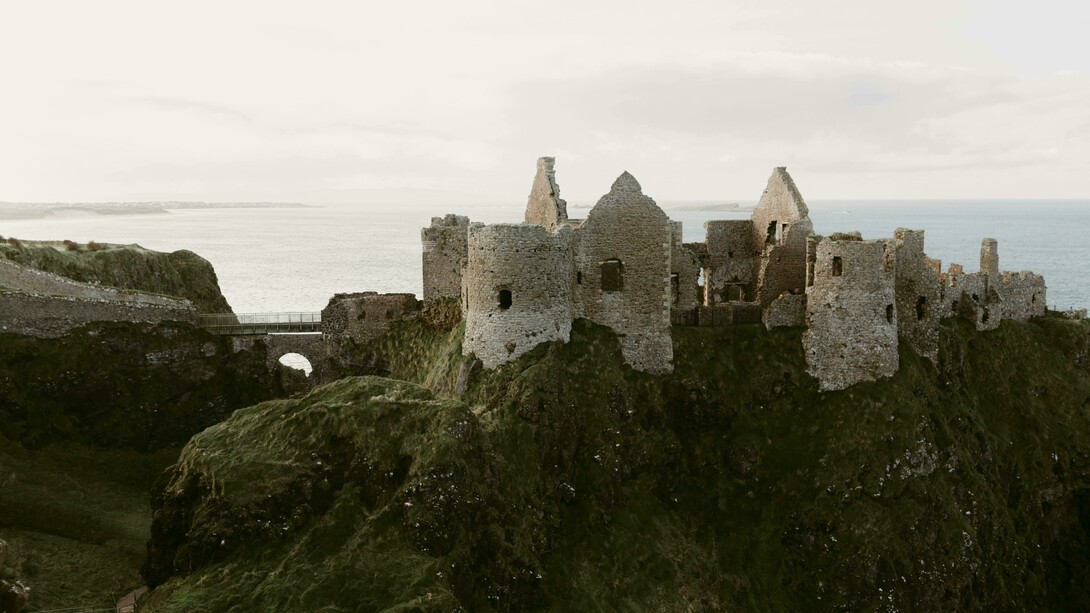 Ruínas medievais do Castelo Dunluce na costa do oceano na Irlanda do Norte, no Reino Unido. Ao final destes dias intensos e cheios de descoberta, regressámos com a sensação de ter conhecido uma Irlanda rica em contrastes — da tranquilidade de vilas junto a lagos às falésias imponentes, das paisagens verdes e rurais às cidades marcadas pela história e pela cultura, bem como pela presença ainda visível da divisão entre a Irlanda Católica e a Irlanda Protestante
