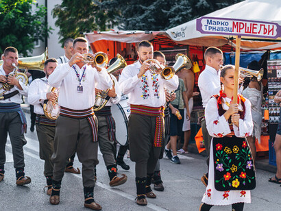 En el Festival de Trompetas de Guča, la participación es un acto de celebración y apoyo a las personas que abren sus puertas, sus cocinas y sus armarios para compartir parte de su identidad con el mundo. Desfile de participantes del Festival de Trompetas de Guča, 2018, Serbia