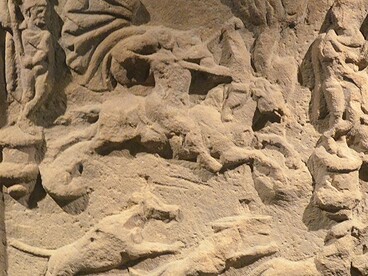 Una raffigurazione di Mitra con una tunica corta e un mantello svolazzante, in sella a un cavallo. Il dio, la cui testa è danneggiata, scaglia una freccia dal suo arco.  Museo Schloss Fechenbach, Dieburg, Germania 