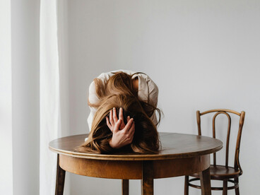 A woman leans on the table, her quiet grief echoed by an empty chair
