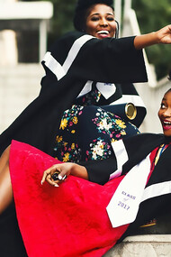 Two women in academic attire pose in graduation robes on the stairs