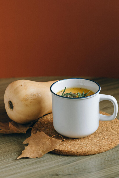 A white ceramic mug holds a steaming winter soup topped with vibrant green herbs