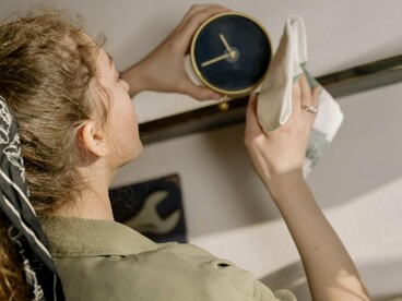 Une femme nettoye une horloge noire posée sur une étagère
