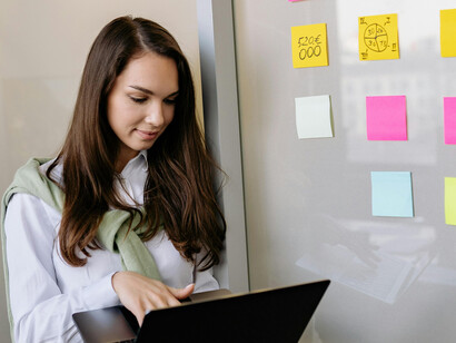 A businesswoman holds a laptop while mentoring a colleague and leading a presentation during a team meeting