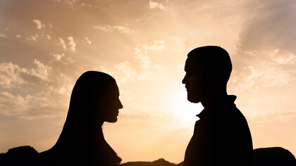 Silhouette di un uomo e una donna che si guardano, con un cielo al tramonto dai colori caldi sullo sfondo