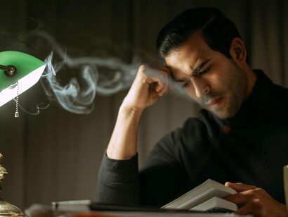 A focused man reading by lamplight late at night, unable to slee