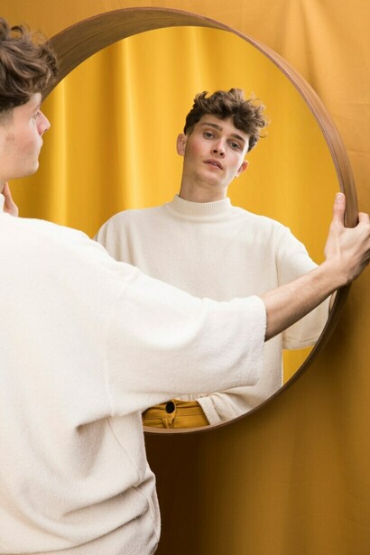 A boy stands in front of a mirror, quietly studying his reflection