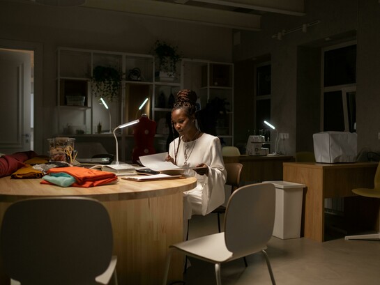 A young African American fashion designer working late in her sewing workspace, a creative professional deep in thought