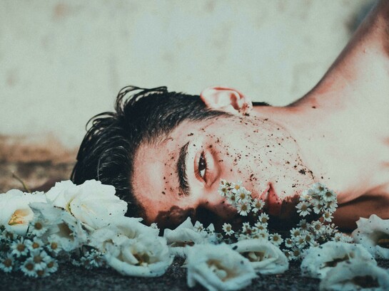 A man lies down next to daisies, looking upset