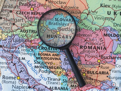 A magnifying glass over European nations illustrates the intense scrutiny needed for the EU to overcome internal bureaucratic hurdles and unify its defense efforts