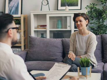 A man and a woman are sitting on a couch, talking to each other