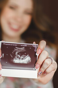 A woman proudly displays her baby's ultrasound photo to the camera