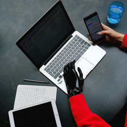 A woman with a prosthetic hand multitasks on her laptop and smartphone, showcasing modern accessibility and innovation
