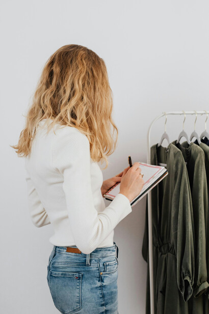A woman in a white long-sleeved top stands beside a clothes rack