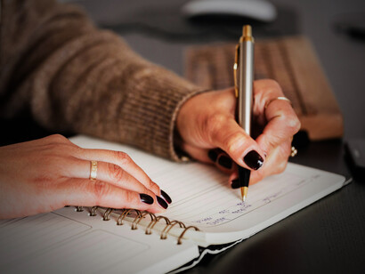 A woman sits quietly, writing notes in her diary with a pen in hand