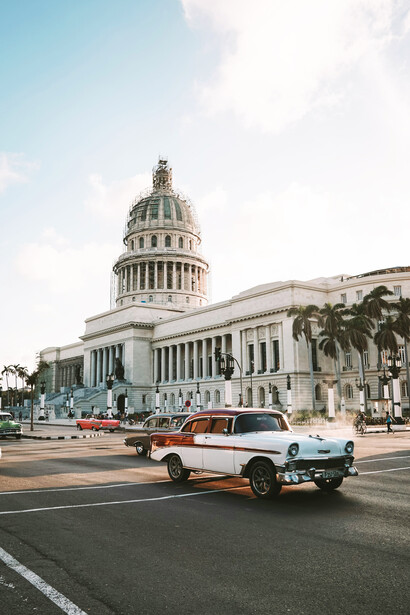 Various vehicles driving on the road with a view of the white-domed historic El Capitolio building in Havana, Cuba, during the daytime