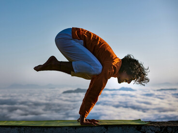 A man practicing yoga on a rooftop ledge against a wide open sky