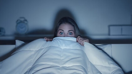 A woman, wrapped in a blanket, enjoying a horror movie with a frightened expression