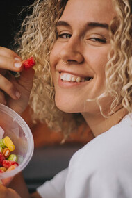 A woman in a white long-sleeve shirt holding a clear plastic container filled with colorful candies
