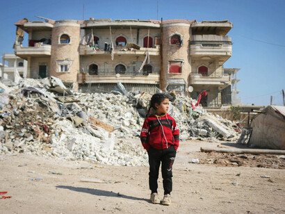 Girl standing in front of war-torn buildings, Idlib, Idlib Governorate, Syria