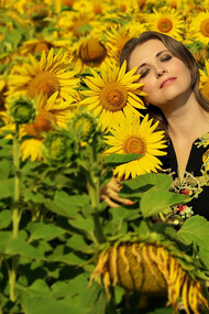 A woman in a black and white floral shirt stands in a sunflower field under the bright daylight, radiating inner peace and a positive mindset
