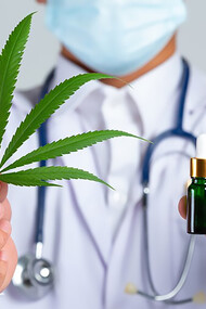 A healthcare professional presenting a cannabis leaf and cannabis oil bottle in front of a white wall, highlighting the therapeutic potential of medical cannabis