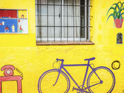 Bicicleta en el mural del artista Gonzalo Prieto, pintado en 2020, en el que se muestran las distintas partes de una casa en un vibrante color amarillo