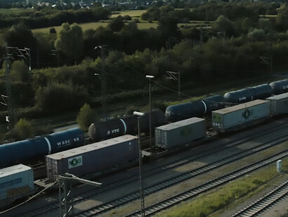 A freight train travels along tracks beside a lush green field, highlighting the transport infrastructure linking Europe and Asia