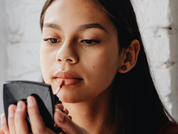 A woman puts on lipstick in front of a mirror, completing her makeup look