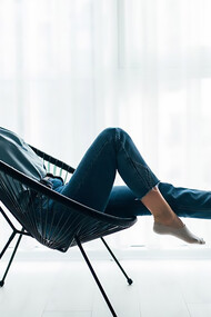 A young woman relaxes in her modern living room, sitting on a stylish chair by the window, embodying the essence of minimalist living
