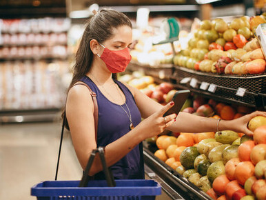 A woman shops for groceries in a supermarket, checking prices on her phone amid rising cost-of-living pressures